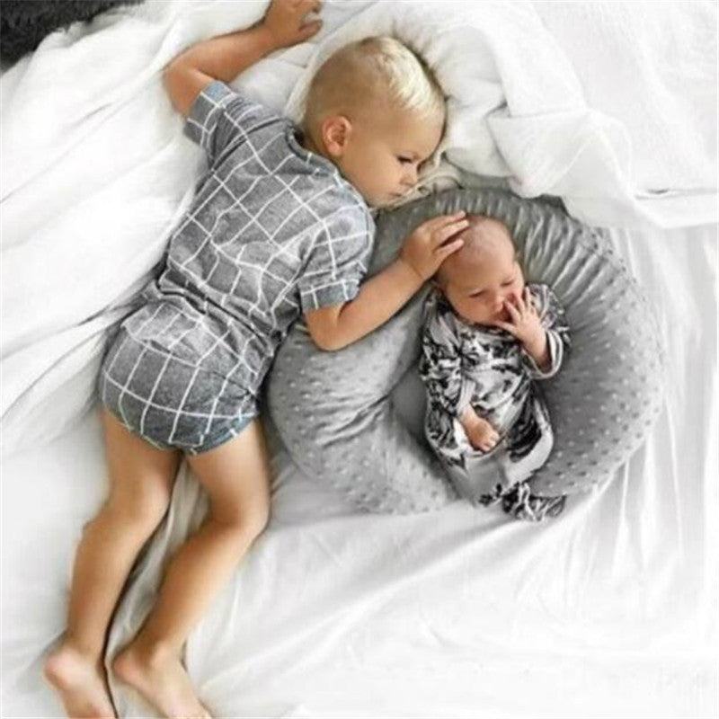 Grand frère allongé près de son petit frère installé dans le coussin d’allaitement Be'Move gris pour un soutien doux et sécurisé