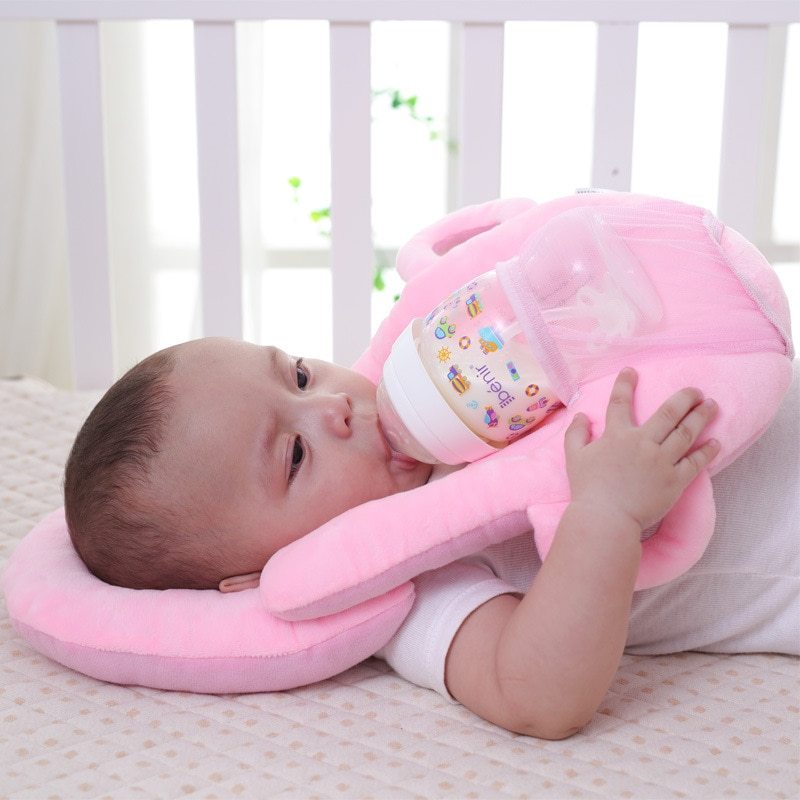 Bébé allongé sur un coussin Be'Tender rose, tenant seul son biberon pour une tétée en toute autonomie et confort.
