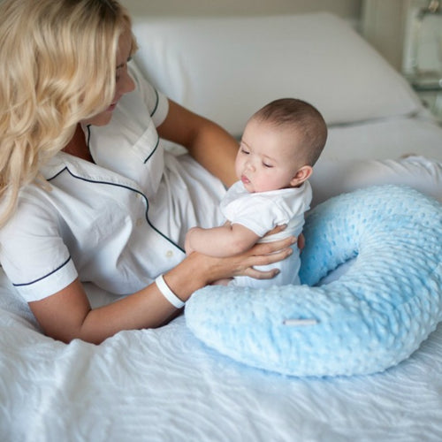 Maman utilisant le coussin d’allaitement portable Be'Move pour soutenir son bébé confortablement sur un lit blanc